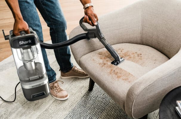 Vacuum cleaning a stained beige couch seat.