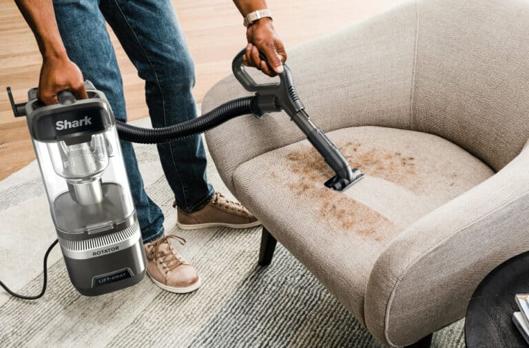 Vacuum cleaning a stained beige couch seat.