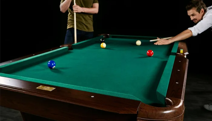 Two people playing pool on green table.
