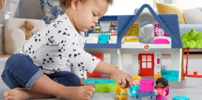 Child playing with dollhouse and figurines on carpet.