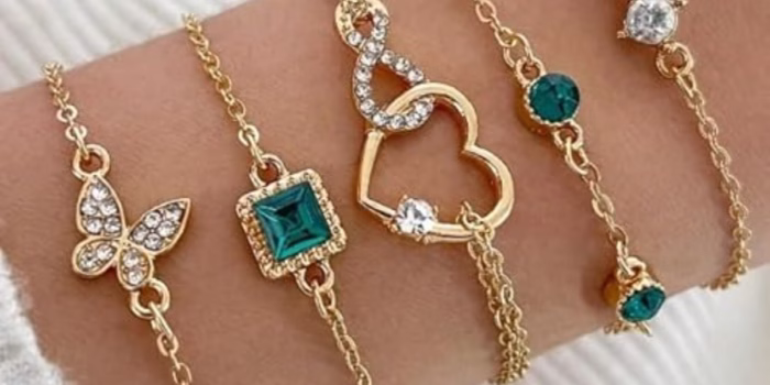 Gold bracelets with charms and gems on wrist.