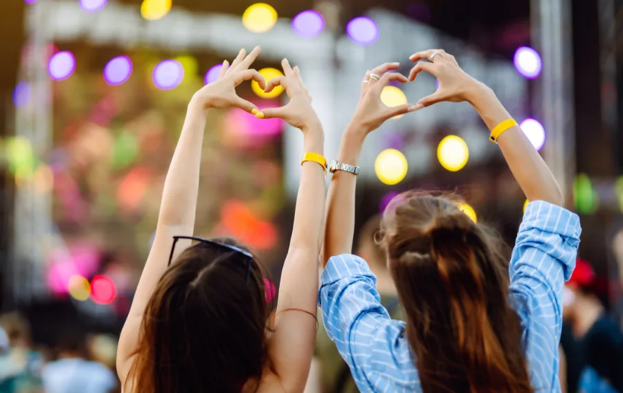 Two people making heart shapes at a concert.