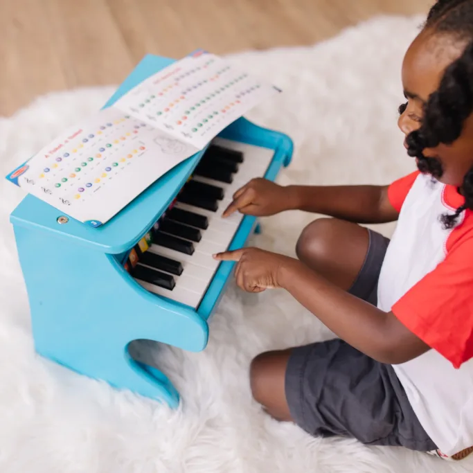 Child playing blue toy piano with music sheet