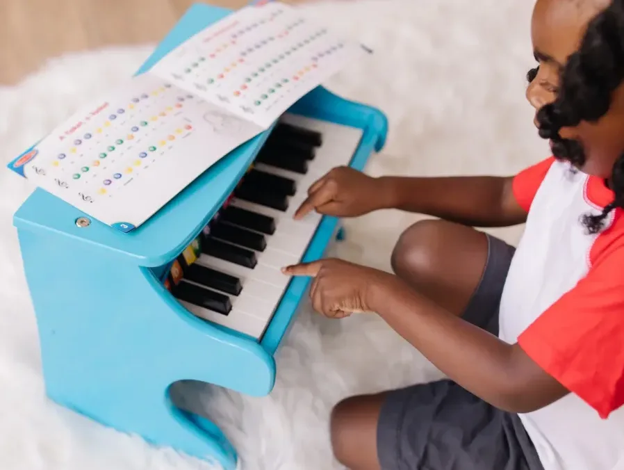 Child playing blue toy piano with music sheet