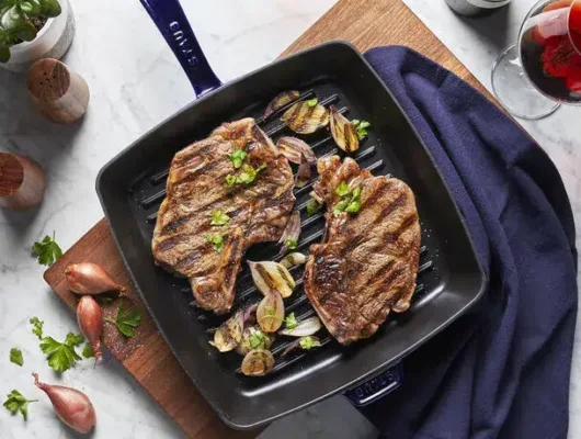 Grilled steaks with herbs in pan on table.