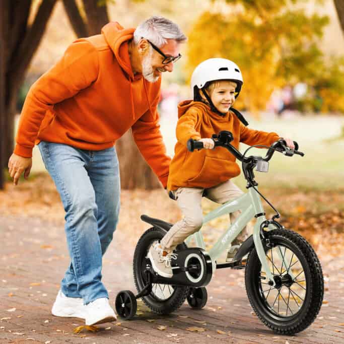 Man helps child ride bike in autumn park.