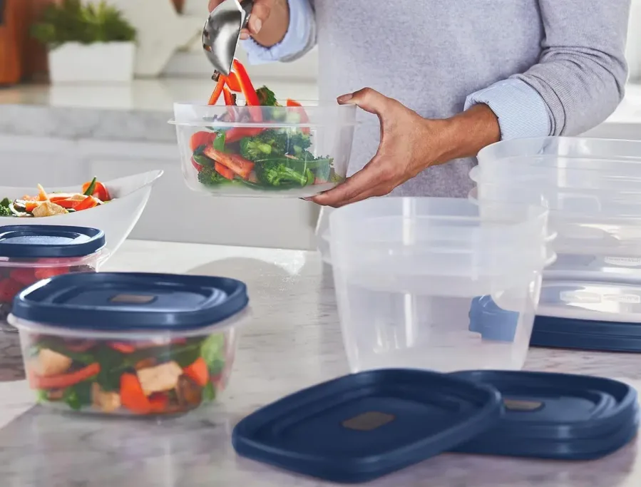 Person filling plastic container with fresh salad.