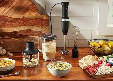 Immersion blender with food and ingredients on kitchen counter.