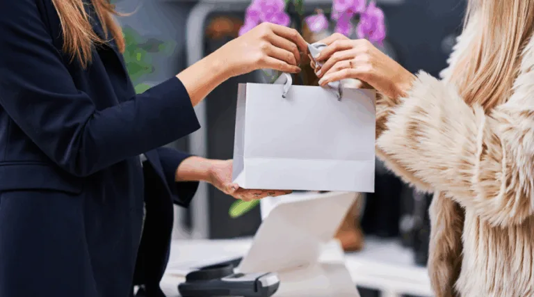 Two women exchanging a shopping bag in store.