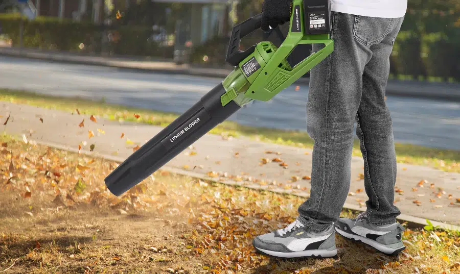 Person using leaf blower on autumn leaves outdoors.