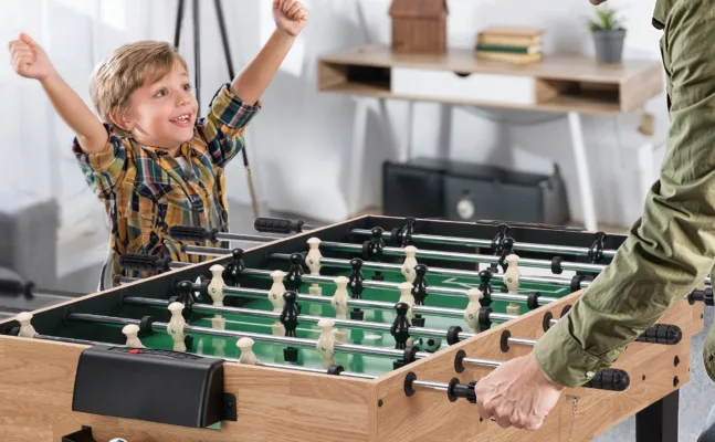Child celebrating foosball game victory enthusiastically.