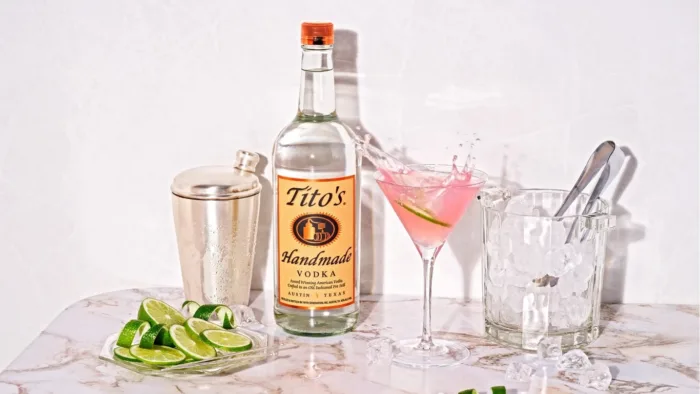 Vodka bottle with cocktail, shaker, ice bucket, and limes.
