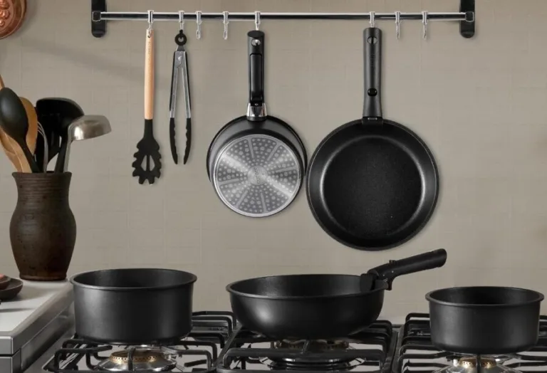 Black cookware set on kitchen stove and hanging rail.
