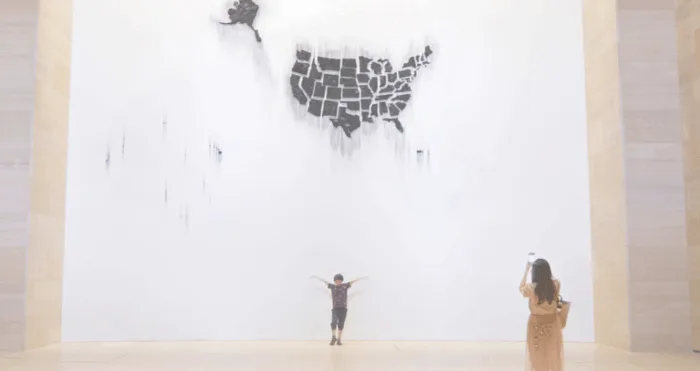 Child posing under abstract US map art installation.