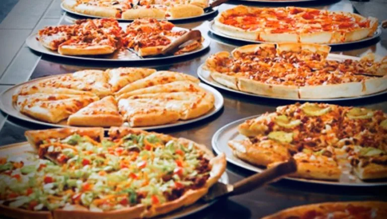 Variety of pizzas on trays at a buffet.
