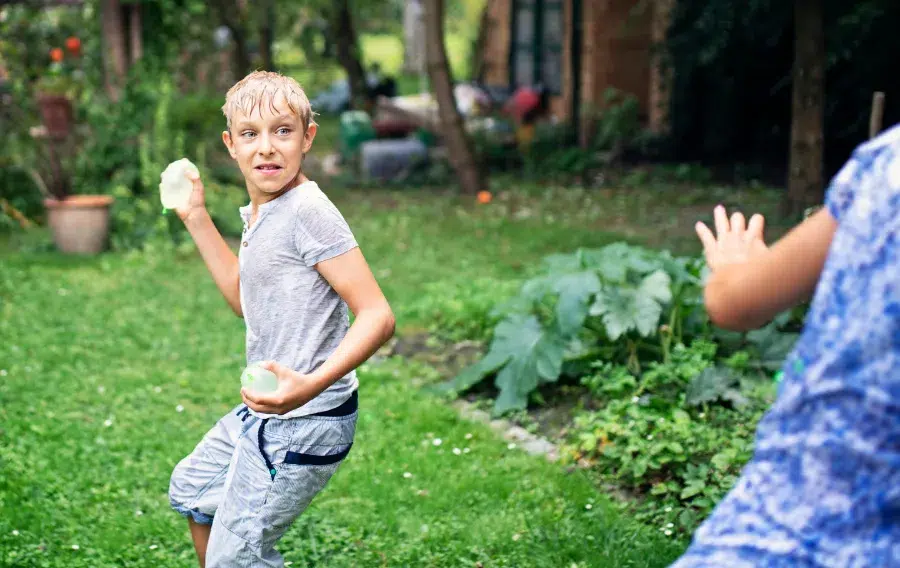 Kids having water balloon fight in garden.