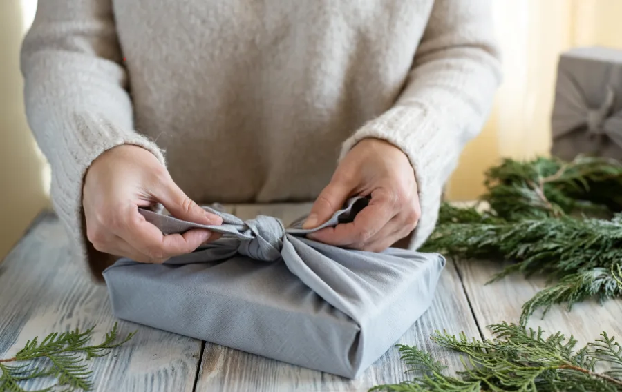Wrapping gift with fabric on wooden table.