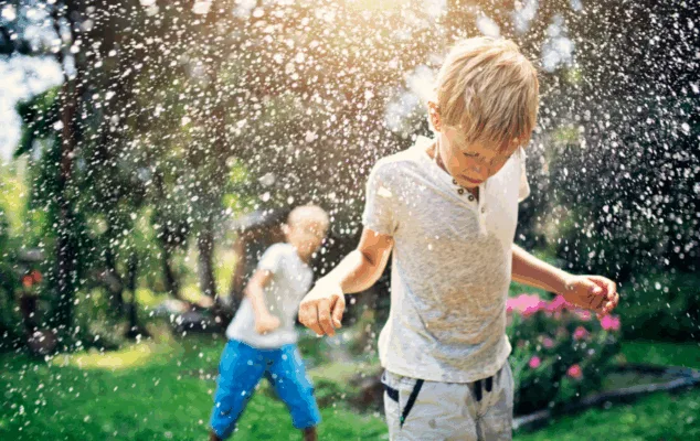 Kids playing in garden sprinkler on sunny day