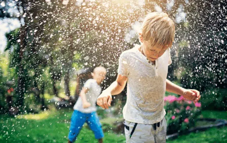 Kids playing in garden sprinkler on sunny day