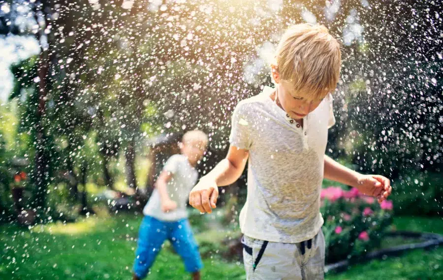 Kids playing in garden sprinkler on sunny day