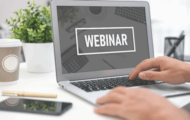 Person typing on laptop, webinar screen displayed.