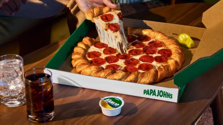 Pepperoni pizza slice, garlic sauce, drinks on table.