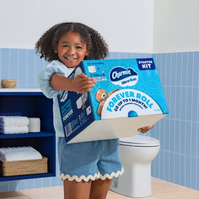 Child holding Charmin toilet paper box in bathroom.