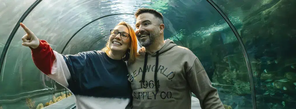 Happy couple exploring underwater aquarium tunnel.