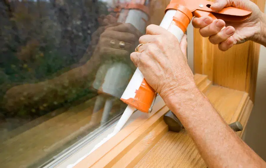 Hands applying caulk to window frame