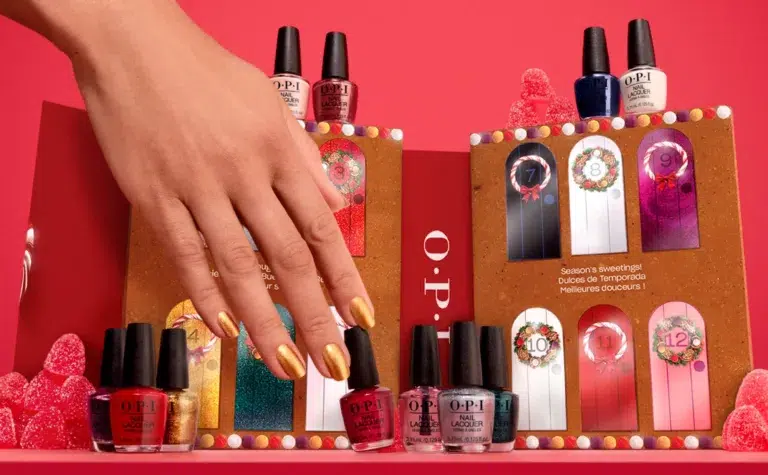 Hand with gold nails, nail polish bottles displayed.
