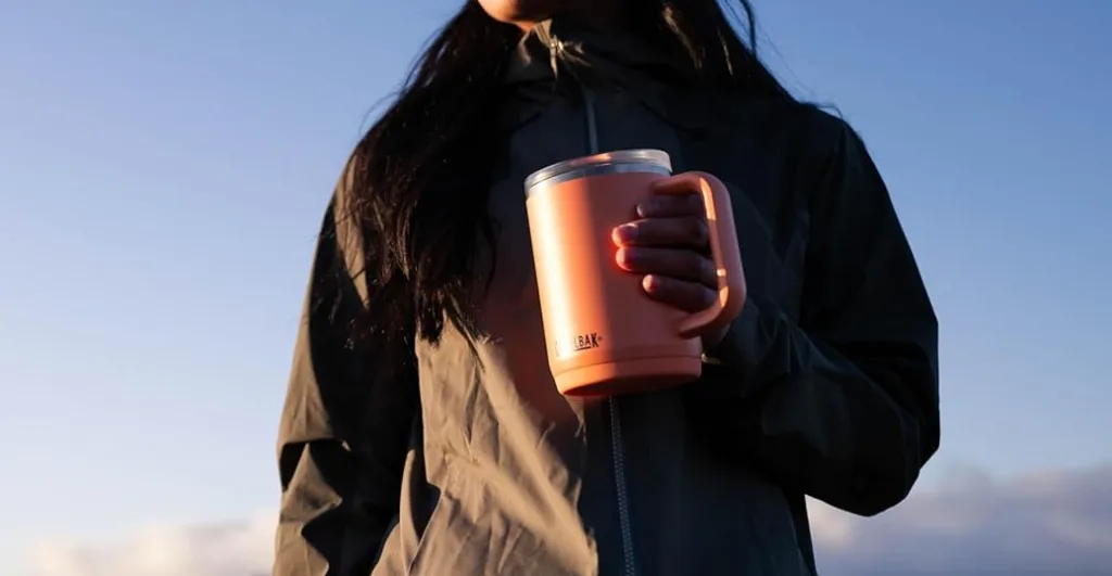 Person holding a pink insulated mug outdoors.