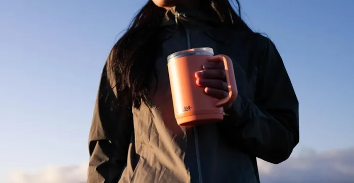 Person holding a pink insulated mug outdoors.
