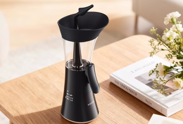 Black coffee grinder on wooden table with flowers.